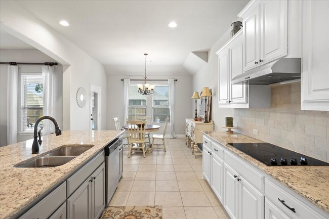 Kitchen with hanging light fixtures, under cabinet range hood, white cabinets, and a sink | Image 16