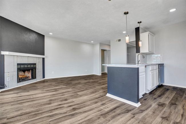 Kitchen featuring white cabinets, hanging light fixtures, decorative backsplash, a fireplace, and dark hardwood / wood-style flooring | Image 5