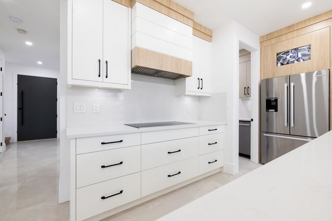 Kitchen with stainless steel refrigerator with ice dispenser, light countertops, custom exhaust hood, recessed lighting, and modern cabinets | Image 14