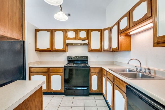 Kitchen featuring black electric range oven, dishwasher, under cabinet range hood, brown cabinetry, and light tile patterned flooring | Image 15