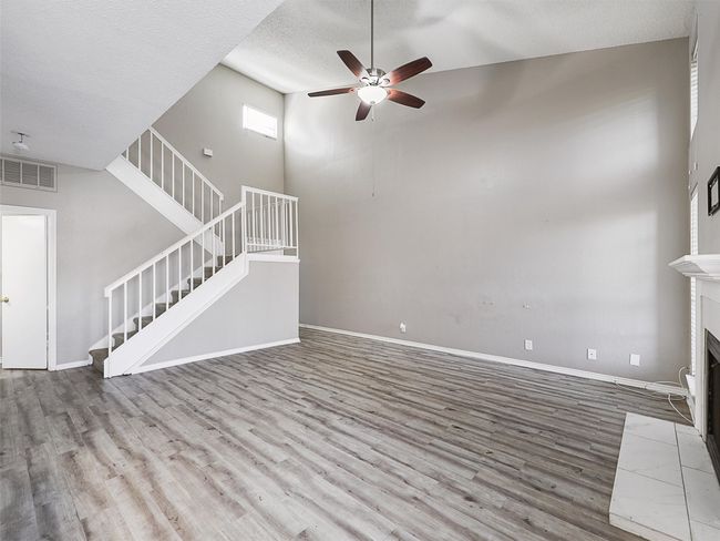 Unfurnished living room with visible vents, baseboards, stairway, wood finished floors, and a ceiling fan | Image 4