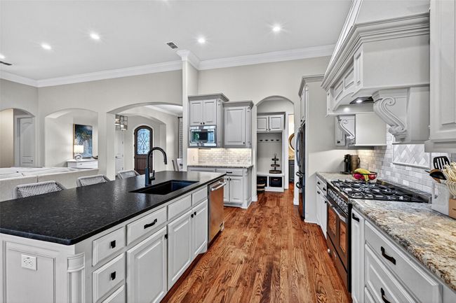 Kitchen featuring stainless steel appliances, arched walkways, a center island with sink, ornamental molding, and wood finished floors | Image 15