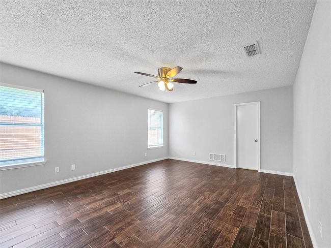 Empty room with ceiling fan, dark wood-type flooring, a textured ceiling, and baseboards | Image 12