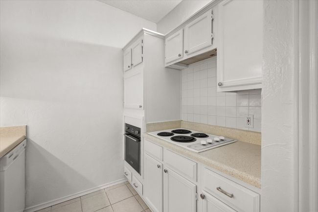 Kitchen featuring white appliances, backsplash, light countertops, light tile patterned flooring, and white cabinets | Image 19