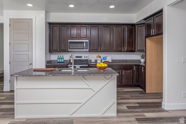 Kitchen with dark stone counters, a sink, appliances with stainless steel finishes, dark brown cabinets, and wood finished floors | Image 5