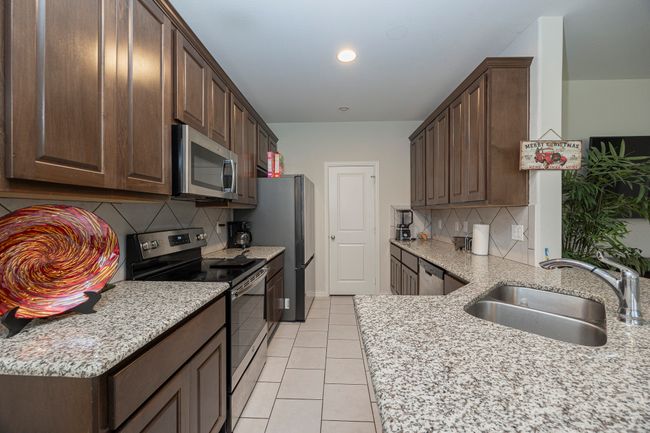 Kitchen with stainless steel appliances, dark brown cabinets, decorative backsplash, light tile patterned flooring, and recessed lighting | Image 13