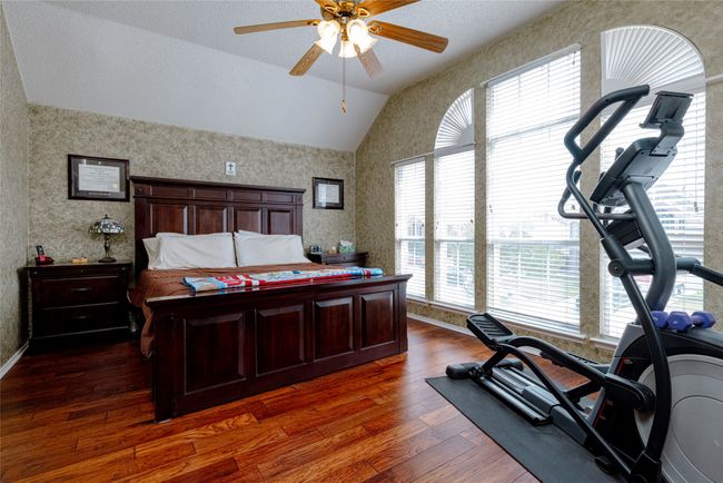 Bedroom with baseboards, ceiling fan, wallpapered walls, dark wood finished floors, and lofted ceiling | Image 21