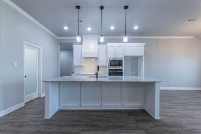 Kitchen featuring stainless steel appliances, crown molding, white cabinets, decorative backsplash, and a spacious island | Image 9
