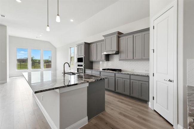 Kitchen featuring gray cabinetry, lofted ceiling, stainless steel appliances, under cabinet range hood, and light wood-type flooring | Image 6