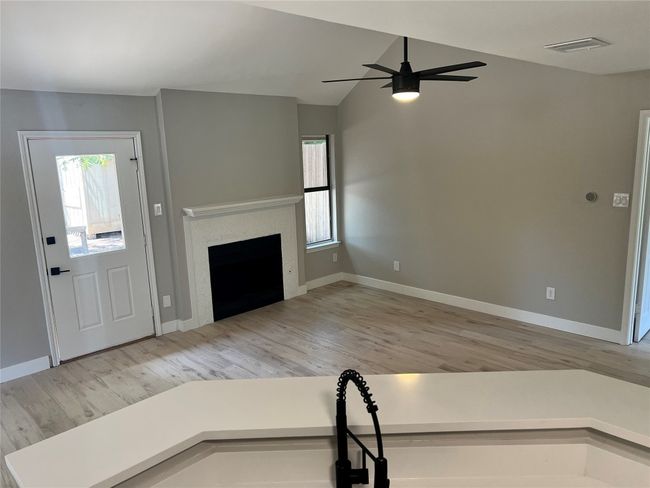 Unfurnished living room featuring wood finished floors, a ceiling fan, a fireplace, and vaulted ceiling | Image 7