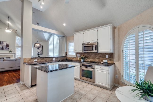 Kitchen with stainless steel appliances, a sink, dark stone counters, ceiling fan, and white cabinets | Image 11