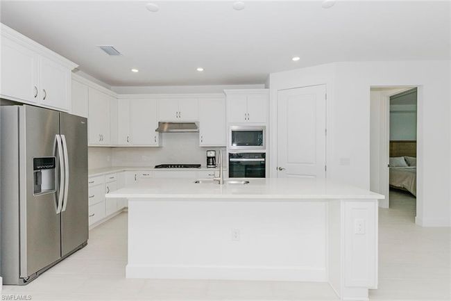 Kitchen featuring black appliances, an island with sink, light countertops, white cabinetry, and recessed lighting | Image 17
