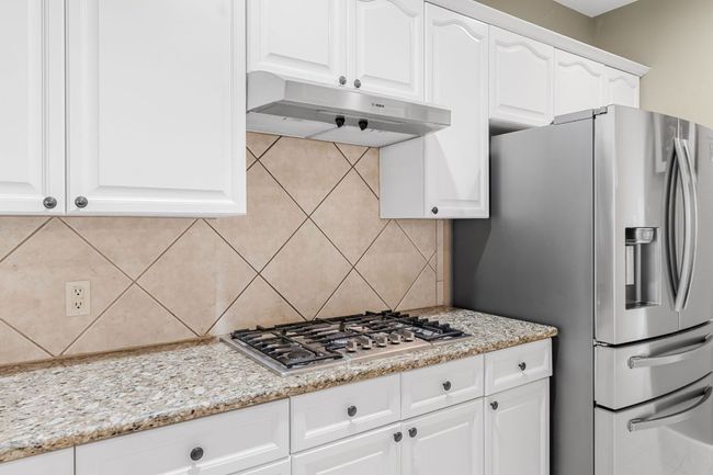 Kitchen featuring under cabinet range hood, appliances with stainless steel finishes, backsplash, white cabinets, and light stone counters | Image 11