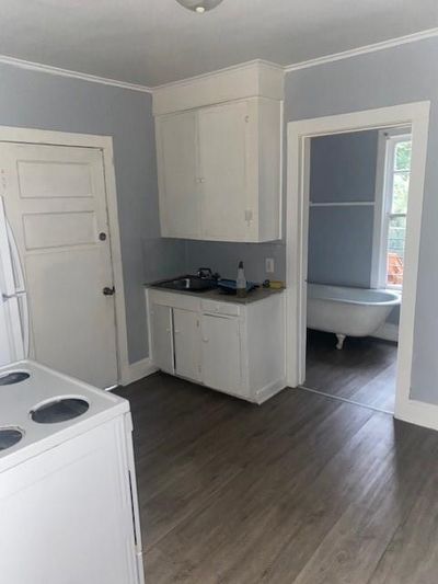 Kitchen with white cabinetry, stove, dark hardwood / wood-style floors, and crown molding | Image 3