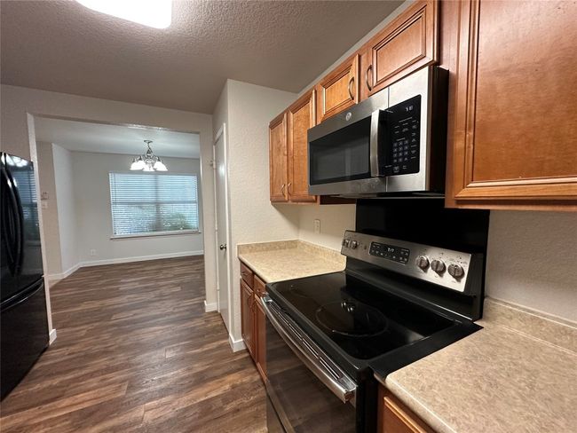 Kitchen with appliances with stainless steel finishes, brown cabinets, dark wood finished floors, a chandelier, and light countertops | Image 16
