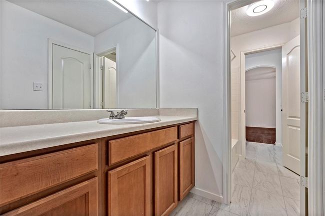 This photo showcases a modern bathroom with a large mirror, wooden cabinetry, and a single sink. The space is well-lit with a sleek ceiling light, and features light-colored flooring, creating a fresh and inviting atmosphere. | Image 29