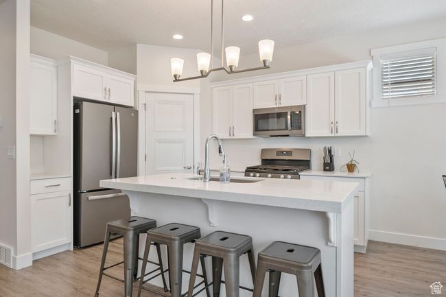 Kitchen featuring appliances with stainless steel finishes, white cabinetry, light wood finished floors, a kitchen bar, and recessed lighting | Image 4