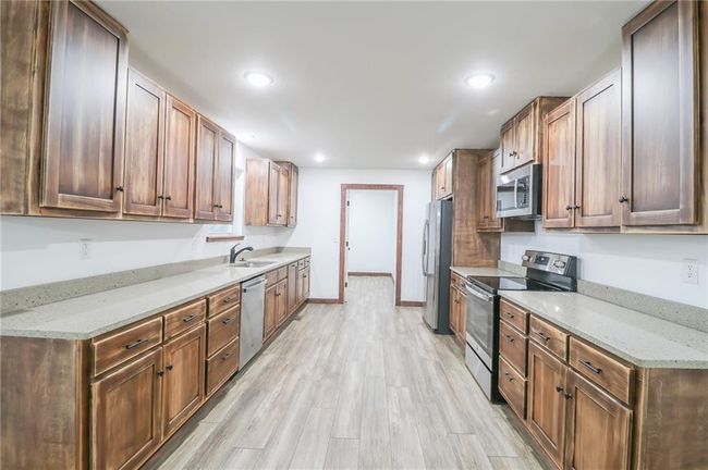 Kitchen featuring appliances with stainless steel finishes, light stone counters, sink, and light hardwood / wood-style flooring | Image 7