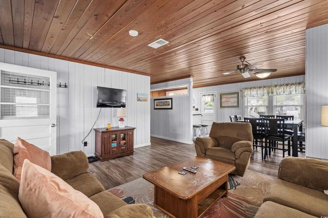 Living room with wood ceiling, a ceiling fan, wood finished floors, baseboards, and wood walls | Image 15