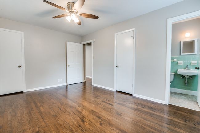 Primary bedroom featuring real wood floors, connected bathroom, tile walls, a sink, and baseboards | Image 21