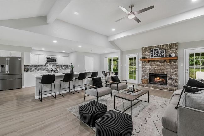 Living room with a ceiling fan, a fireplace, vaulted ceiling with beams, and light wood-style flooring | Image 4