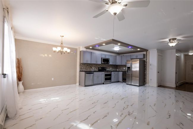 Kitchen with greyish countertops, ceiling fan with notable chandelier, baseboards, and appliances with stainless steel finishes | Image 6