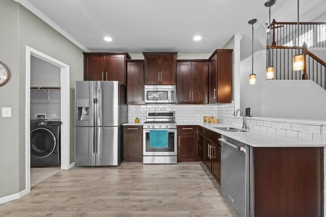 Kitchen with appliances with stainless steel finishes, washer / clothes dryer, a sink, backsplash, and dark brown cabinetry | Image 15