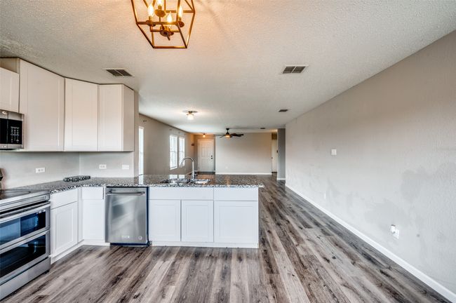 Kitchen with appliances with stainless steel finishes, a sink, a peninsula, wood finished floors, and white cabinets | Image 11