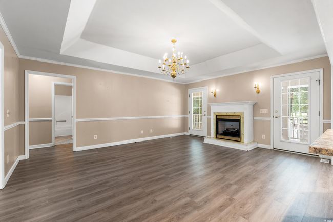 Unfurnished living room featuring a tray ceiling, a chandelier, dark wood finished floors, and crown molding | Image 16