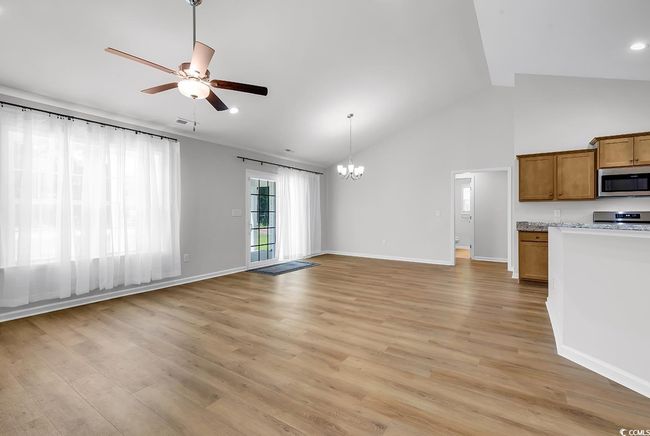 Unfurnished living room with a chandelier, a ceiling fan, light wood-style flooring, baseboards, and high vaulted ceiling | Image 6