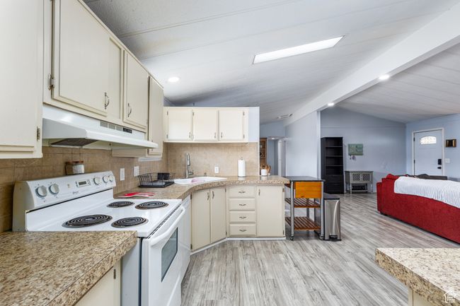 Kitchen with lofted ceiling with beams, electric range, under cabinet range hood, light countertops, and a sink | Image 8
