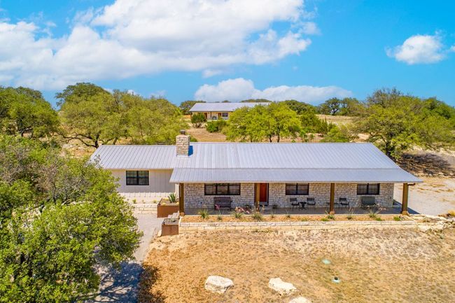 Ranch-style home featuring a chimney, a porch, metal roof, and stone siding | Image 12