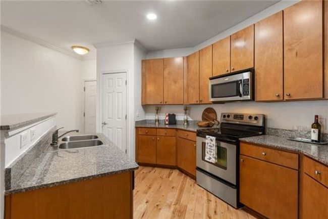 Kitchen with appliances with stainless steel finishes, a sink, brown cabinets, light wood-style floors, and ornamental molding | Image 5