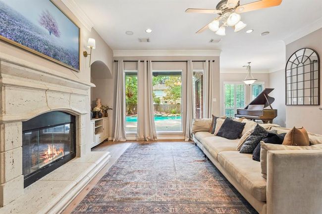 This inviting living room features a cozy fireplace. Natural light floods in through glass doors, offering a view of the backyard and pool. The space combines elegance and comfort, perfect for relaxation and entertaining. | Image 6