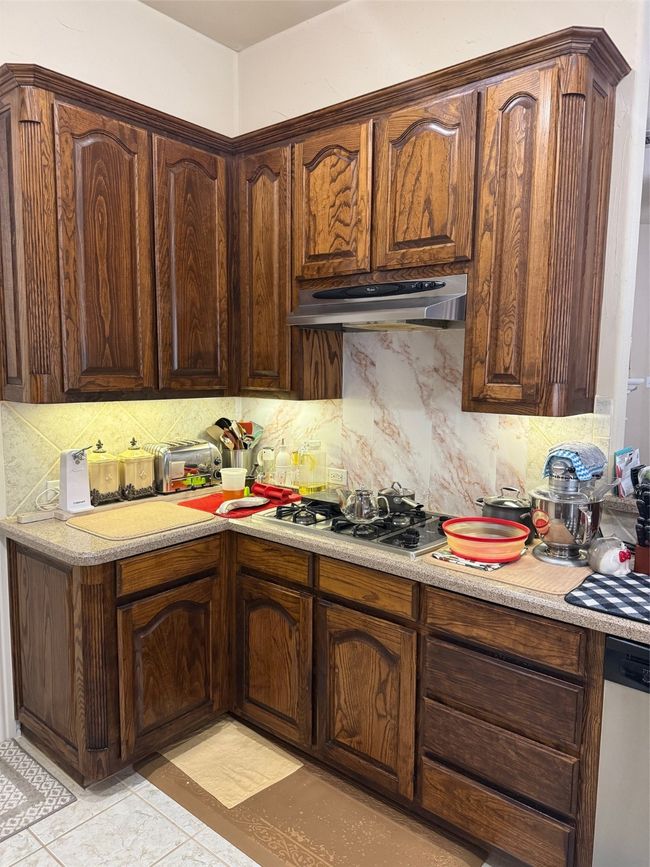 Kitchen featuring stovetop, range hood, tasteful backsplash, light countertops, and dishwashing machine | Image 18