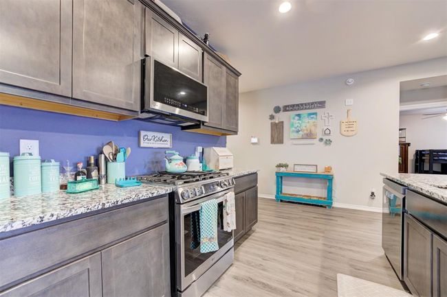 Kitchen featuring appliances with stainless steel finishes, dark brown cabinetry, light stone counters, light wood-style flooring, and recessed lighting | Image 16