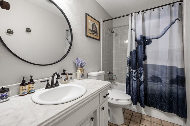 Full bath featuring tile patterned floors, a textured wall, toilet, vanity, and shower / bath combo with shower curtain | Image 22