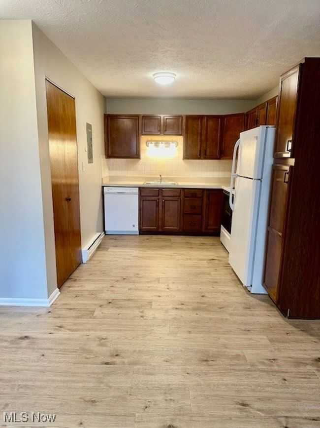 Kitchen featuring white appliances, light wood finished floors, a baseboard radiator, a sink, and backsplash | Image 6