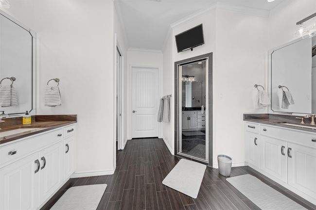 Full bath featuring a shower stall, two vanities, ornamental molding, and wood tiled floors | Image 10