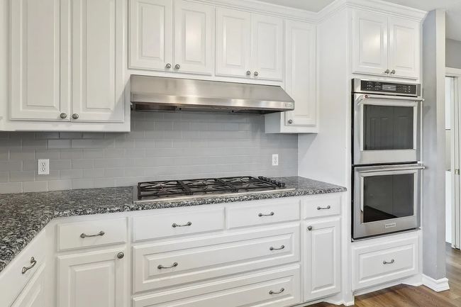 Kitchen featuring wood finished floors, stainless steel appliances, tasteful backsplash, under cabinet range hood, and white cabinetry | Image 8