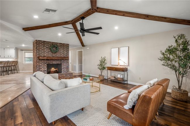 Living room with baseboards, visible vents, lofted ceiling with beams, hardwood / wood-style floors, and a fireplace | Image 12
