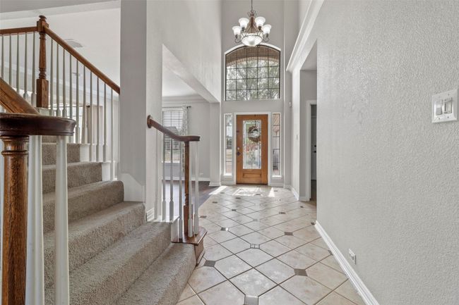 Foyer entrance featuring a textured wall, a high ceiling, a chandelier, light tile patterned floors, and stairs | Image 6