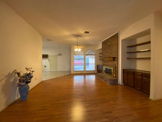 Unfurnished living room featuring wood finished floors, ceiling fan, a fireplace, and built in features | Image 7