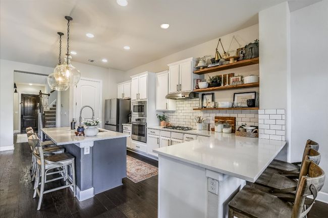 Kitchen with a sink, appliances with stainless steel finishes, a kitchen breakfast bar, under cabinet range hood, and white cabinetry | Image 8