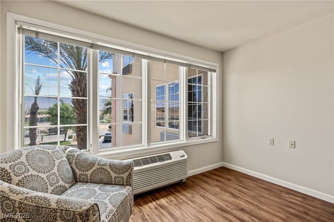 Sitting room with an AC wall unit, wood finished floors, and baseboards | Image 12