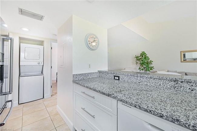Kitchen featuring stacked washer and dryer, white cabinetry, visible vents, light tile patterned flooring, and light stone countertops | Image 12