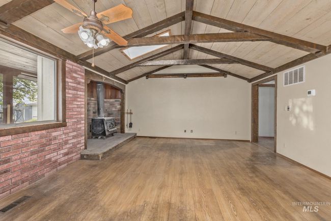 Unfurnished living room featuring a wood stove, wood finished floors, a ceiling fan, wooden ceiling, and brick wall | Image 5