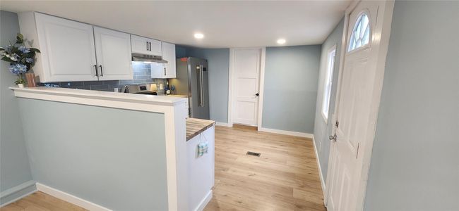 Kitchen featuring tasteful backsplash, baseboards, light wood-type flooring, under cabinet range hood, and recessed lighting | Image 9