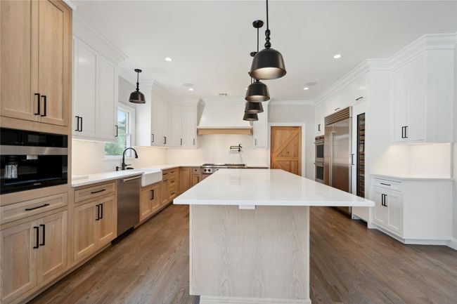 Kitchen featuring appliances with stainless steel finishes, custom exhaust hood, dark wood-style floors, a center island, and light countertops | Image 14