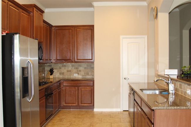 Kitchen with black appliances, a sink, stone counters, decorative backsplash, and ornamental molding | Image 11